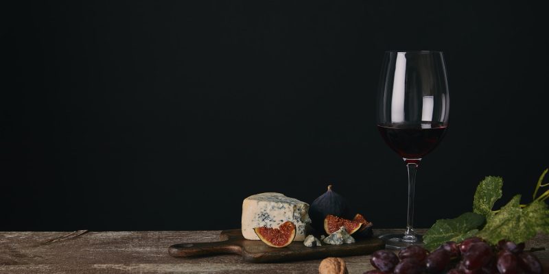 glass of red wine, cheese and fresh fruits on wooden table